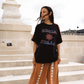 Model wearing Kinga Csilla Sunset Tee in black with sun logo, styled with Bello Swirl Jessi Pants featuring embroidered floral details, standing on stone steps in Paris