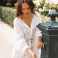 Woman wearing the Kinga Csilla Tottori Lace Harlow Maxi Dress in white embroidered cotton, washing hands at a Parisian fountain surrounded by roses.