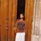 Woman wearing Kinga Csilla Tottori Lace Ode Skirt – white cotton lace maxi skirt styled with oversized brown Lino Roses long sleeve tee in Paris street style look