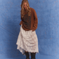 Model wearing Kinga Csilla Tottori Lace Ode Skirt, white lace maxi skirt styled with oversized brown Lino Roses Tee and black boots, studio photoshoot with blue backdrop