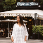 Woman wearing the Kinga Csilla Tottori Lace Pia Mini in white lace, styled with scalloped hem and embroidery, photographed in Paris street style outside Café de Flore.
