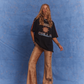 Model in Kinga Csilla Twilight Velvet Flare Pant in golden velvet with KC logo side stripe, styled with oversized Kinga Csilla Sunset tee, photographed against a textured blue backdrop.