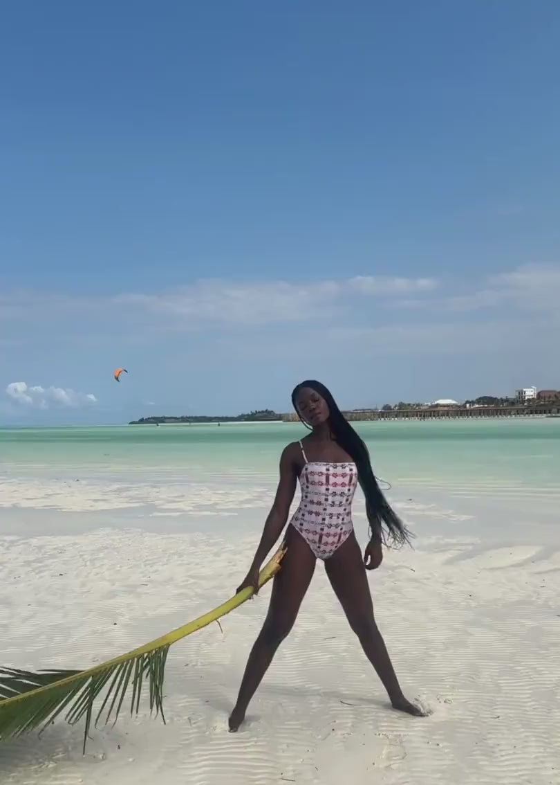 Woman wearing pink patterned one-piece in tropical setting. 